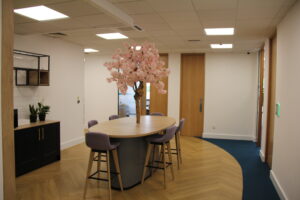 A modern office breakout area with a cherry blossom centrepiece, bar stools, and a collaborative work table.